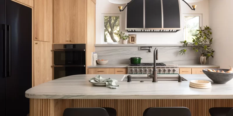 Scandinavian-style kitchen with Taj Mahal Quartzite countertops, light wood cabinetry, and a black range hood, featuring a sleek, minimalist design.