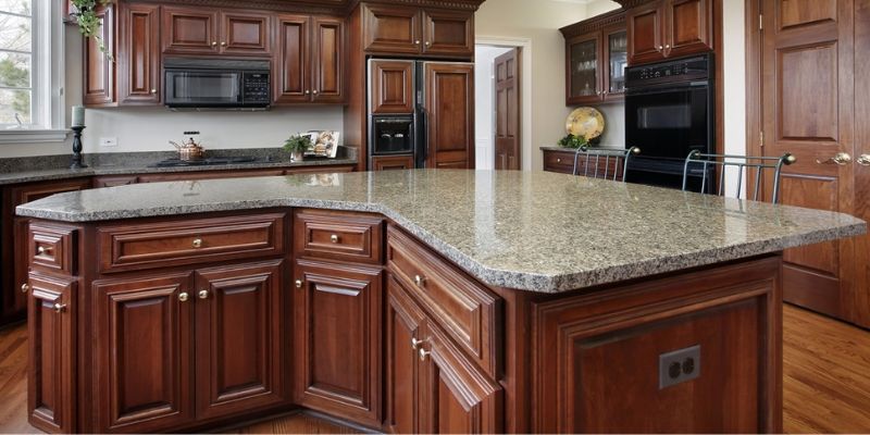 Traditional kitchen with rich, dark wood cabinetry and a large granite countertop island, featuring subtle speckling and a polished finish. The kitchen includes built-in appliances and a warm, classic design style.