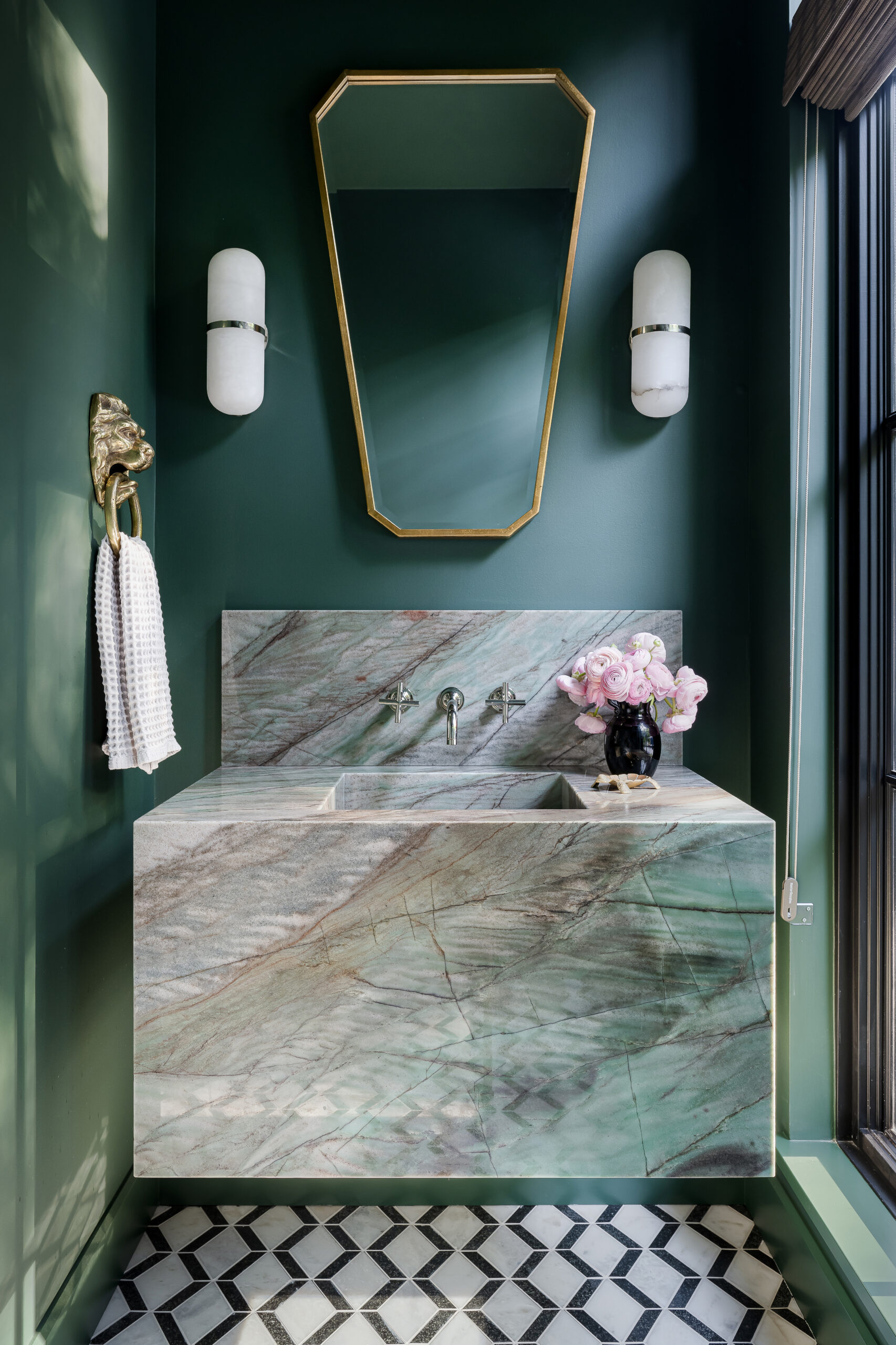 Nothing grounds a moody powder room like a bold vanity and integrated sink made of natural stone. The  veining in marble or quartzite can add instant texture and depth, creating a centerpiece that’s both functional and beautiful. In our first example, a rich, veined quartzite vanity is paired with deep green walls. This color choice amplifies the stone’s  visual impact, letting the veins pop against the darker background. More subtle undertones within the quartzite are able to shine in this stylish powder room. 